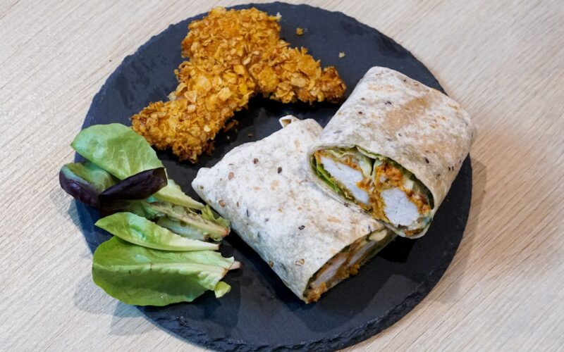 a black plate topped with a burrito and a salad